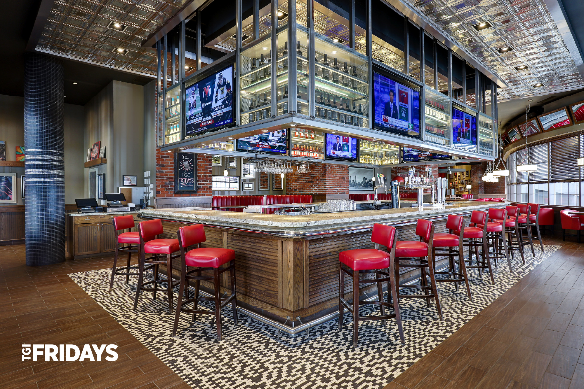 TGI Fridays restaurant bar with tall, red bar stools. Bar with multiple seats and television screens visible from all seats.
